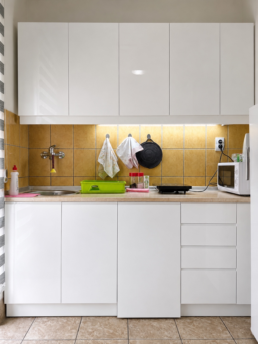 Bela kuhinja u apartmanu MIRAX sa sudoperom, indukcionom pločom, mikrotalasnom i frižiderom