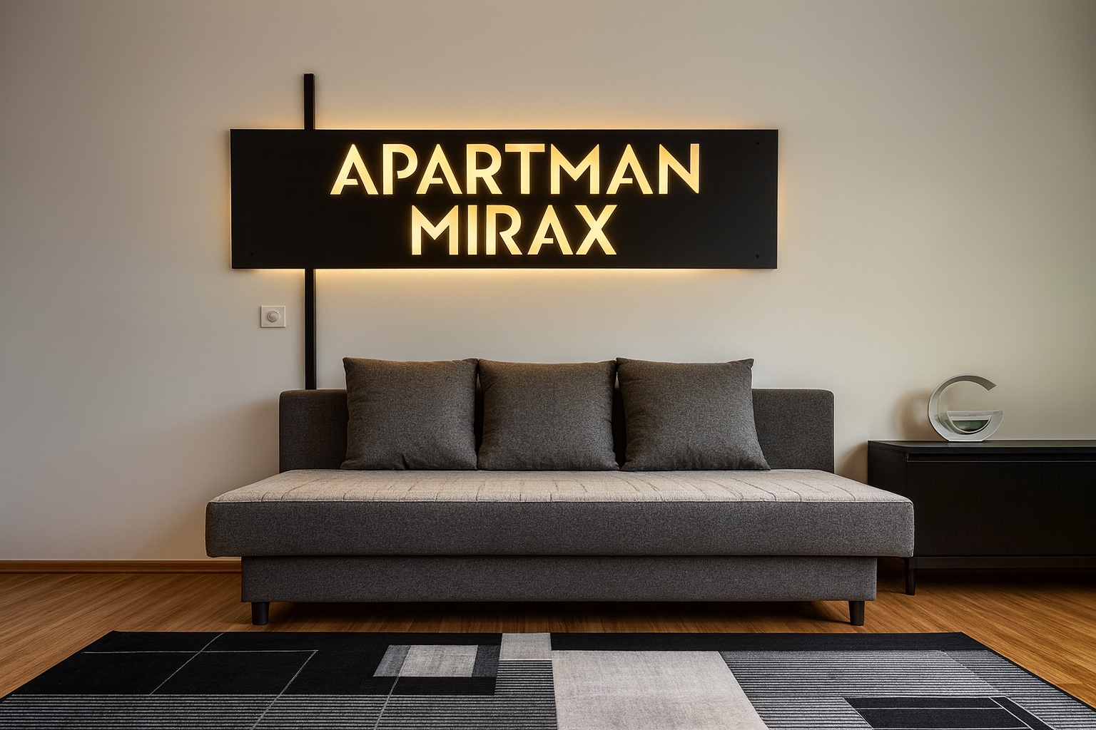 Siva sofa ispod osvetljenog natpisa Apartman MIRAX u dnevnom boravku